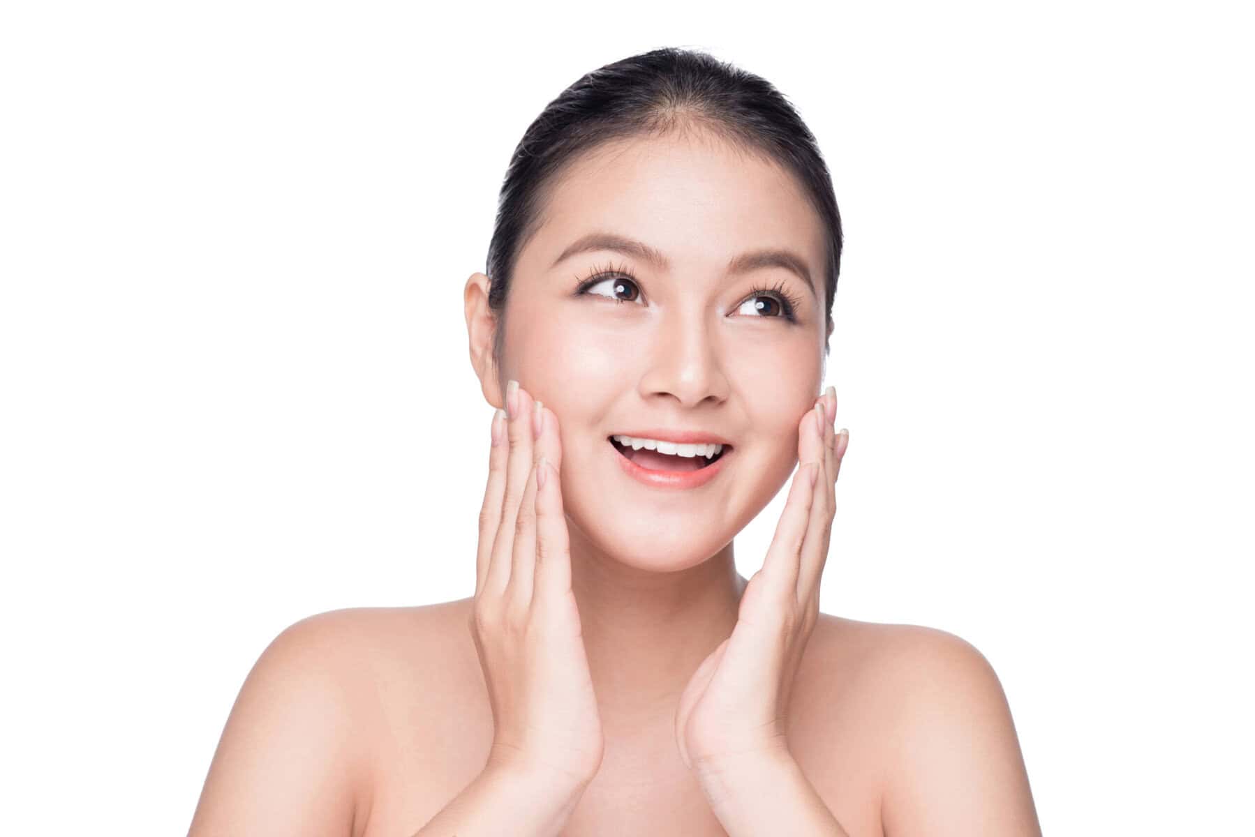 Clear-skinned young woman touching her face, smiling, with glowing skin.