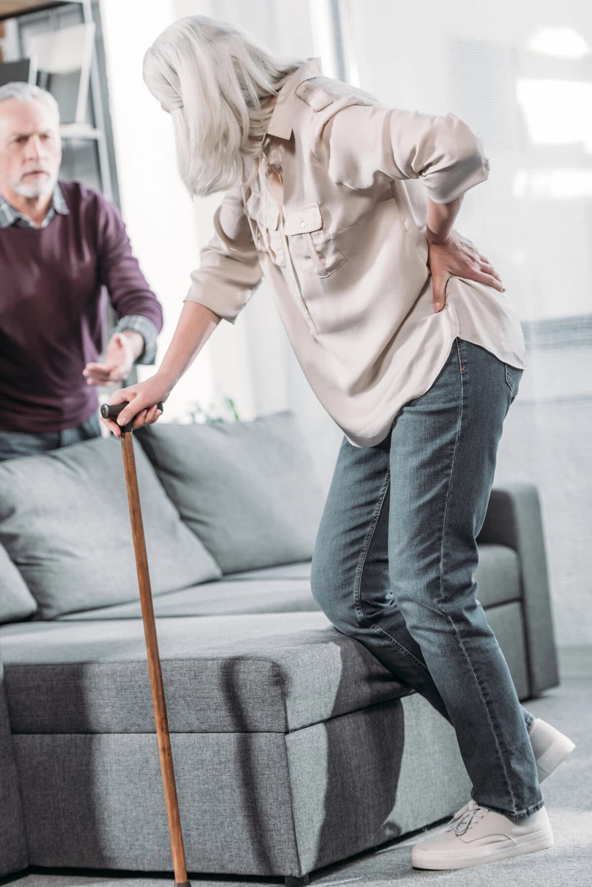 Carrying elderly woman with back pain holding cane on sofa, seeking medical help, healthcare, pain relief.