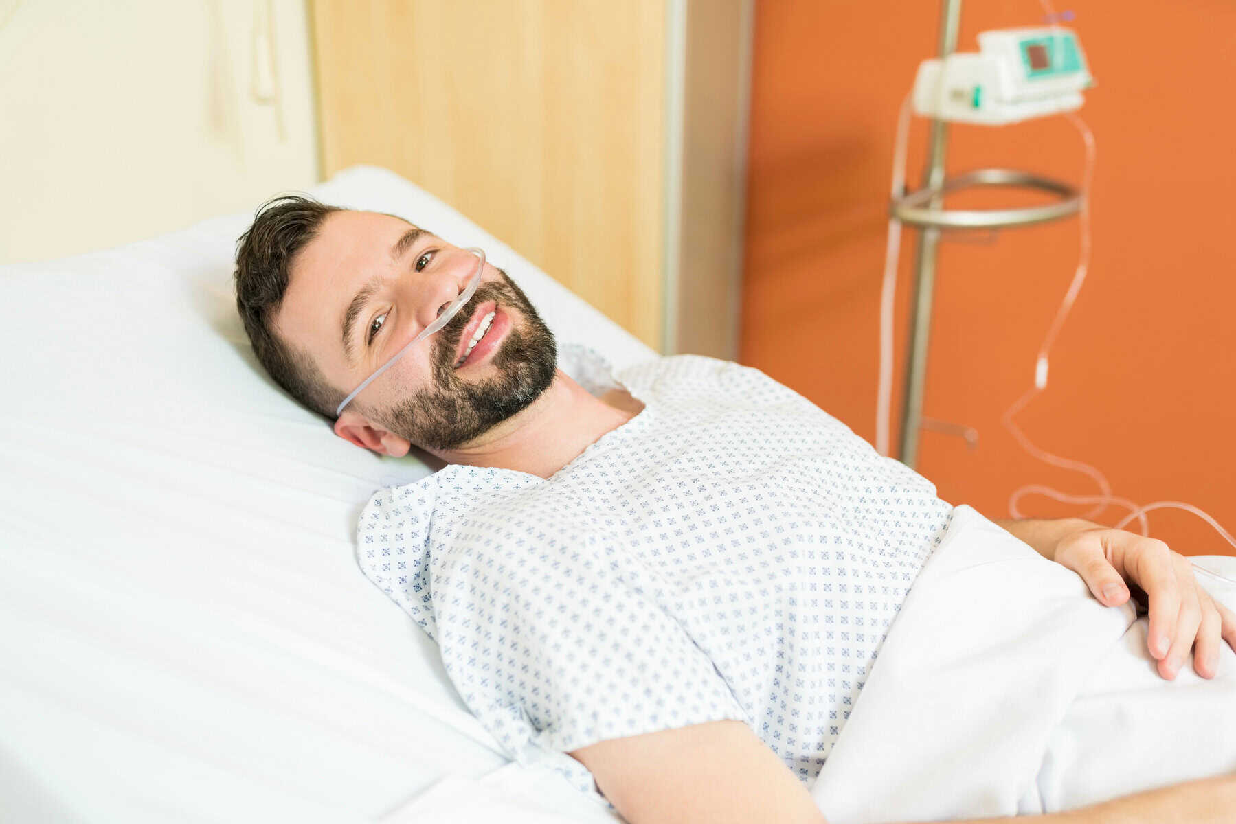 Depositphotos_326084552_XL Healthy man smiling in hospital bed with oxygen, patient undergoing treatment.